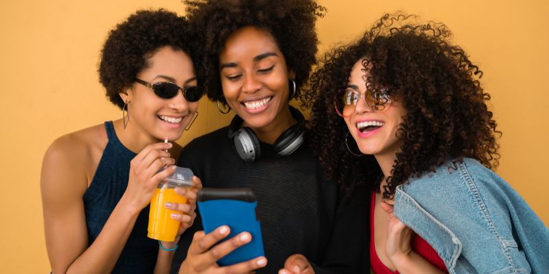 group of three young women smiling while looking at a smartphone